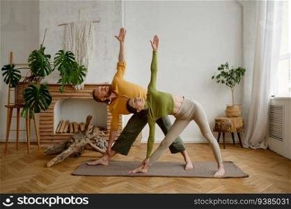 Young man and woman couple practicing yoga together standing in Trikonsana triangle pose. Healthy lifestyle and sport daily routine concept. Young man and woman couple practicing yoga together standing in triangle pose