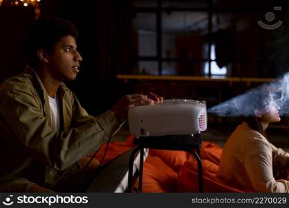 Young man and woman couple preparing to watch movie film on domestic tv projector at home. Young couple preparing to watch movie film
