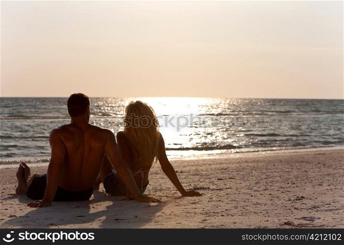 Young Man and Woman Couple Sitting on Beach At Sunset