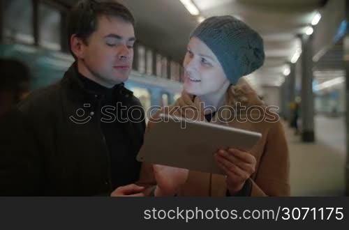 Young man and woman discussing some issue using tablet computer. They talking at underground station, arriving train in background