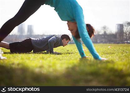 Young man and woman doing push up training on playing field