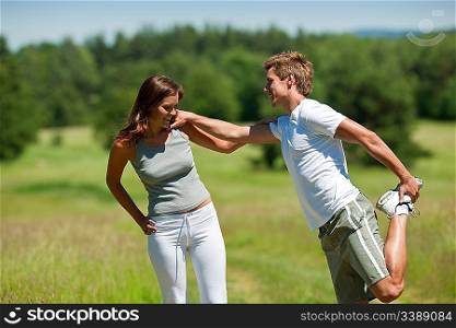 Young man and woman exercising in spring meadow on sunny day