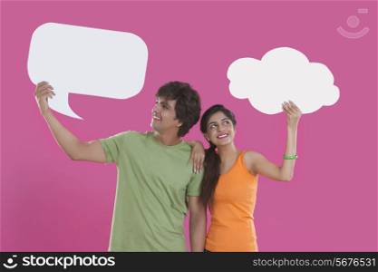 Young man and woman holding communication bubbles over pink background