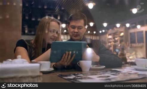 Young man and woman in a cafe looking on the touchpad and talking vividly