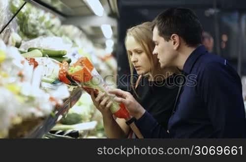 Young man and woman in grocery choosing fresh vegetables, checking them at first