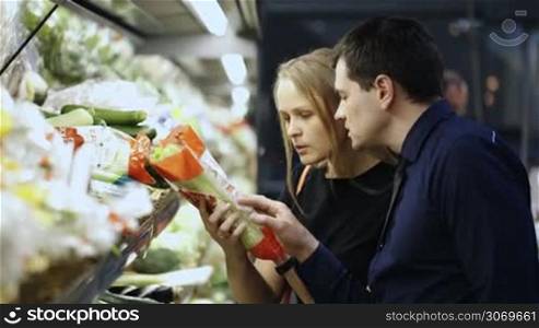 Young man and woman in grocery choosing fresh vegetables, checking them at first