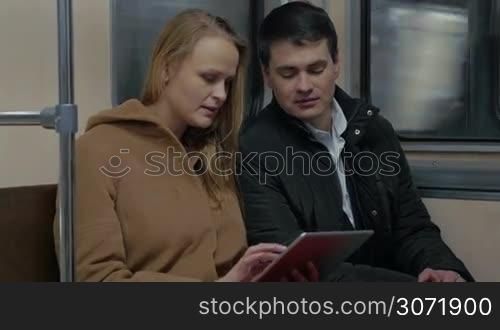 Young man and woman in moving underground train. They using pad and talking during the ride