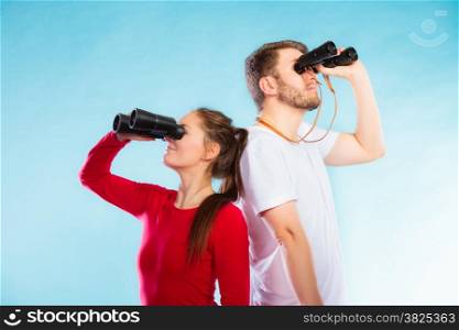 Young man and woman lifeguards on duty or tourist couple looking through binocular studio shot on blue