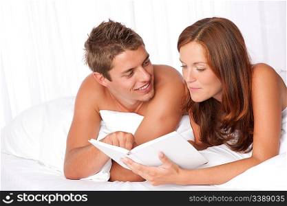 Young man and woman lying down on white sofa, woman reading book