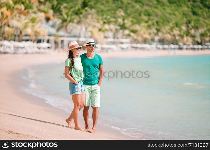 Young man and woman on the beach during summer vacation. Happy lovers enjoy their honeymoon at exotic island. Young couple walking on tropical beach with white sand and turquoise ocean water at Antigua island in Caribbean