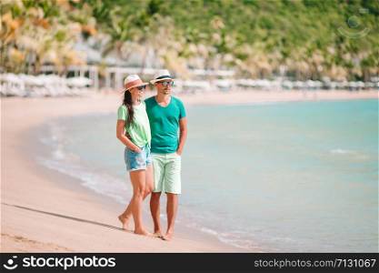 Young man and woman on the beach during summer vacation. Happy lovers enjoy their honeymoon at exotic island. Young couple walking on tropical beach with white sand and turquoise ocean water at Antigua island in Caribbean