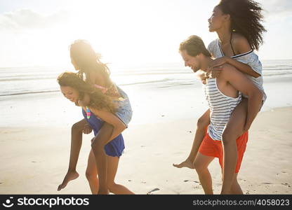Young man and woman piggybacking friends in beach race, Cape Town, South Africa