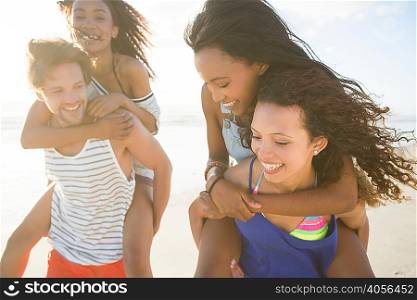 Young man and woman piggybacking friends on beach, Cape Town, South Africa