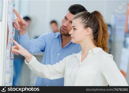 young man and woman pointing at bulletin board