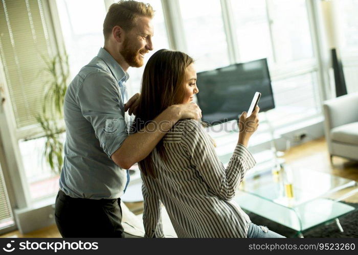 Young man and woman standing embraced in the room and using mobile phone