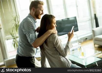 Young man and woman standing embraced in the room and using mobile phone