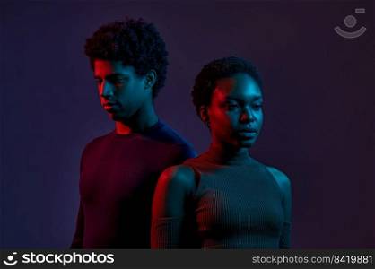 Young man and woman standing together in neon light over dark background, concept of human emotions, facial expression, fashion, beauty. Young man and woman in neon light over dark background