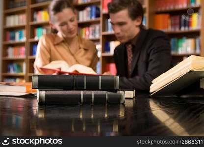 Young man and woman studying at desk in library, focus on books in foreground