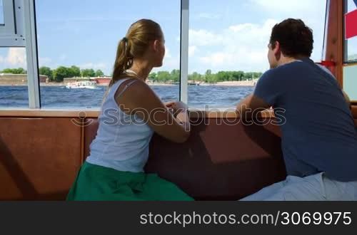 Young man and woman traveling by tourist boat on river. They enjoying panorama and talking