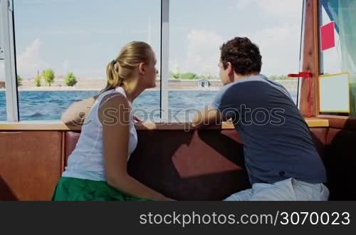 Young man and woman traveling by touristic boat. They talking and looking at sights around