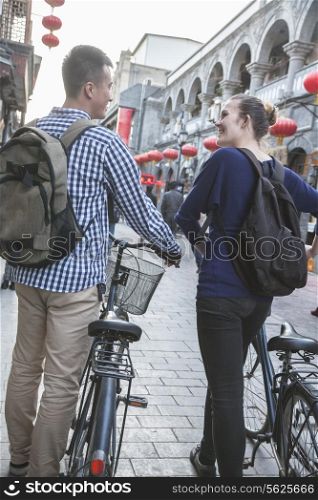 Young man and woman with bicycles, walking down street.