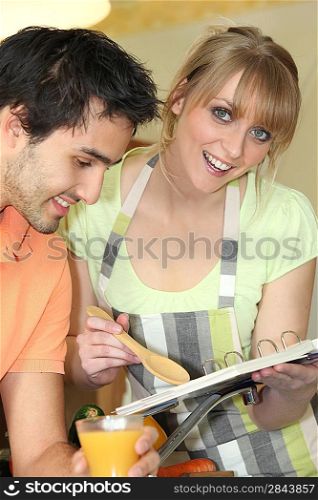 Young man and young smiling while reading cookbook