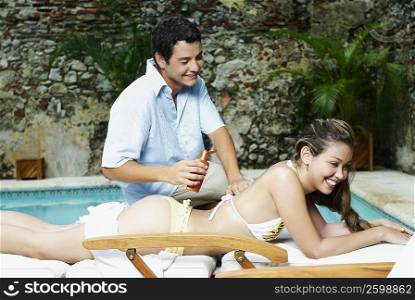 Young man applying suntan lotion on a young woman&acute;s back at the poolside