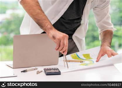 Young man architect or engineer working at desk with designer equipment to make interior design at workplace. Real estate business and civil engineering concept.
