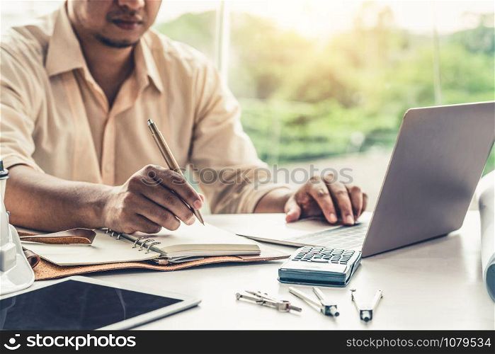 Young man architect or engineer working at desk with designer equipment to make interior design at workplace. Real estate business and civil engineering concept.