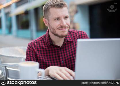 Young Man At Outdoor Cafe Working On Laptop