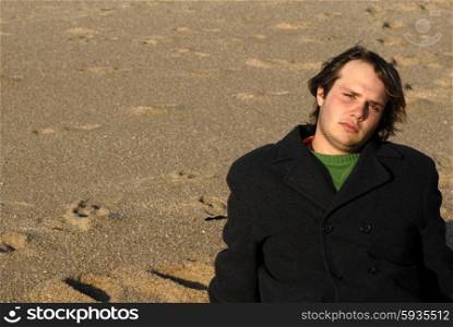 young man at the beach seated in the sand