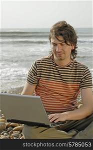 young man at the beach with laptop