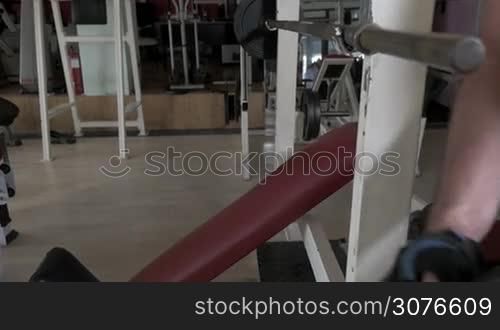 Young man at the gym, hang up damn to rod and then lies on bench and doing exercise chest press with rod