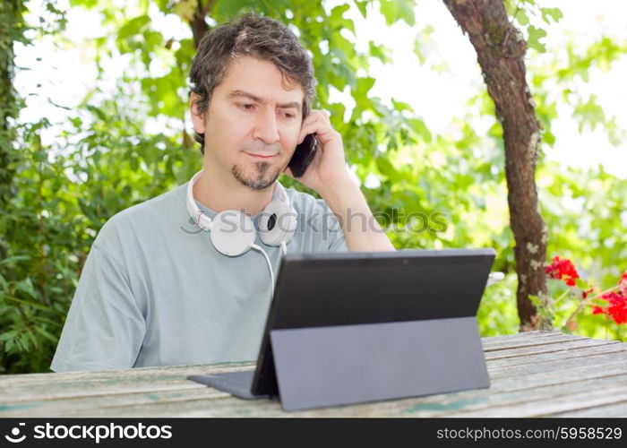 young man at the phone and tablet pc with headphones, outdoor