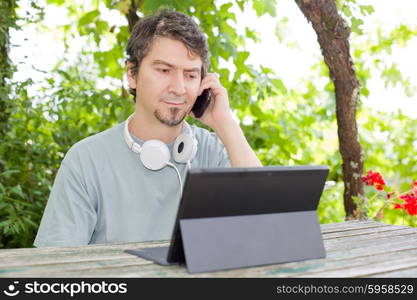 young man at the phone and tablet pc with headphones, outdoor