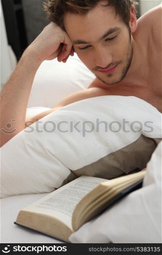 young man bare-chested reading in bed