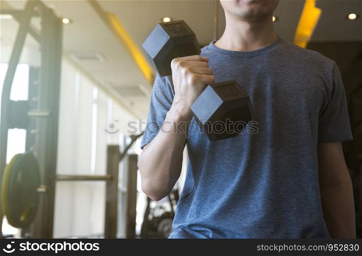 Young man beginner exercising with dumbbell flexing muscles at gym, sport training concept