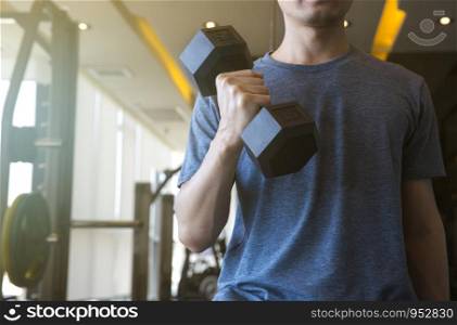 Young man beginner exercising with dumbbell flexing muscles at gym, sport training concept