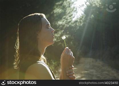 Young man blowing dandelion in forest
