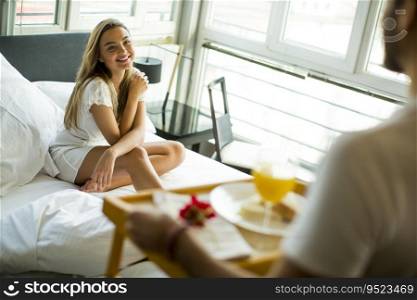 Young man brings breakfast in bed to young girl