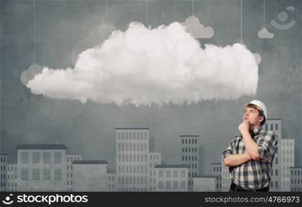 Young man builder looking thoughtfully at cloud in sky. Idea concept. Builder has an idea