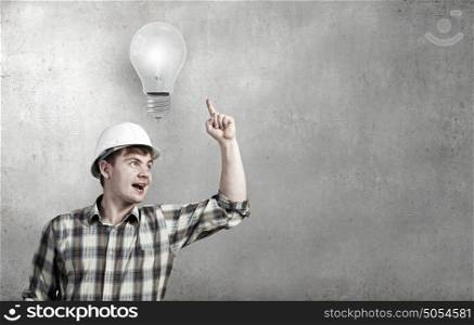Young man builder looking thoughtfully at light bulb. Idea concept. Builder has an idea