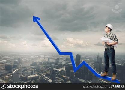 Young man builder standing on graph and looking at city. Builder has an idea