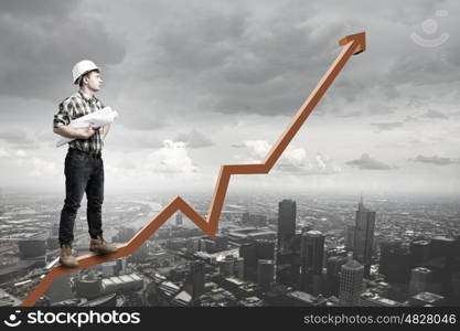 Young man builder standing on graph and looking at city. Builder has an idea