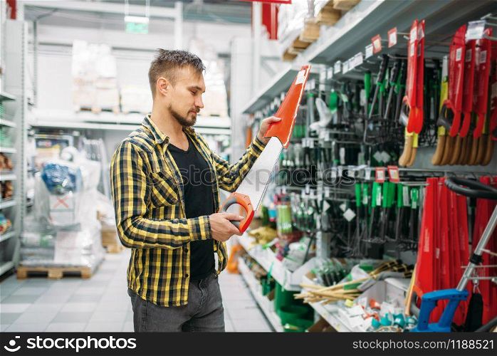 Young man buying saw in supermarket. Male customer on shopping in hypermarket, tools department