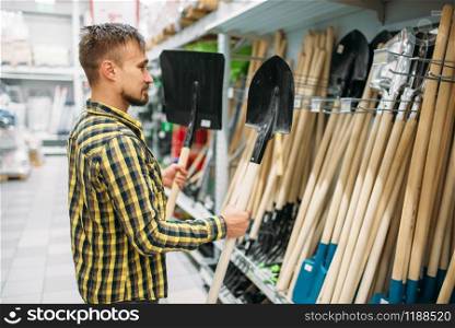 Young man buying shovel in supermarket. Male customer on shopping in hypermarket, tools department