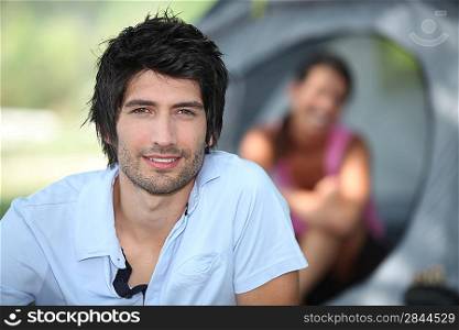 Young man camping with his girlfriend and tent out of focus in the background
