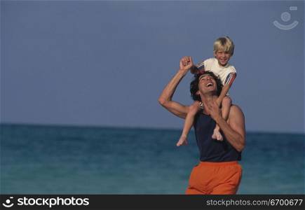 Young man carrying a boy on his shoulders on the beach