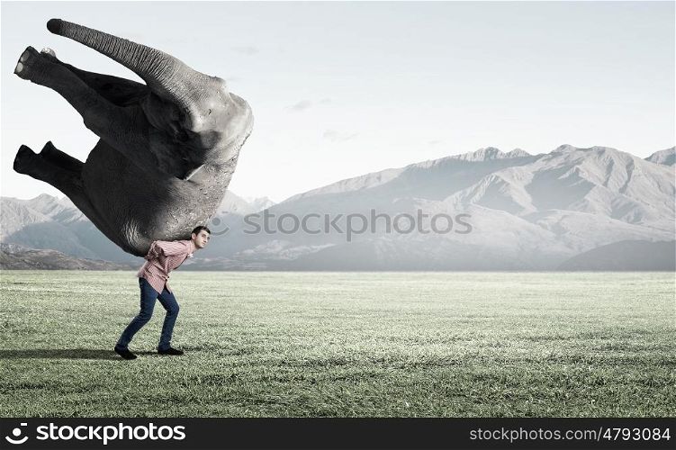 Young man carrying heavy elephant on his back. Big weight is not problem