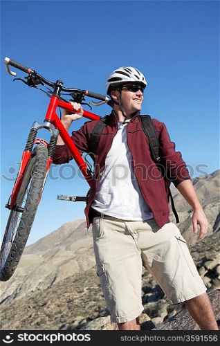 Young Man Carrying Mountain Bike in front of hills